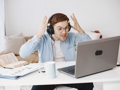 Man med hörlurar som lyfter händerna i frustration framför en bärbar dator
