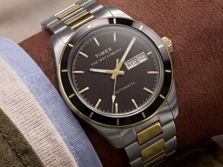 En tvåfärgad Timex Waterbury Heritage Automatic med svart urtavla bärs på handleden och visar dag- och datumvisning samt guldtonade detaljer.