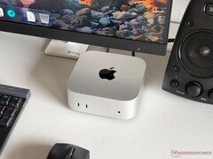 En Apple M6 Mac mini på ett skrivbord i en speluppsättning med skärm, tangentbord, mus och högtalare.