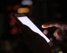 En hand som håller en smartphone med en upplyst skärm i mörkret