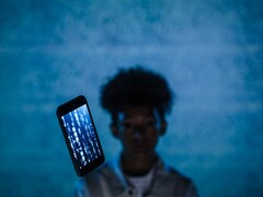 Svävande smartphone med kod på skärmen framför en blå bakgrund, med en suddig person bakom den
