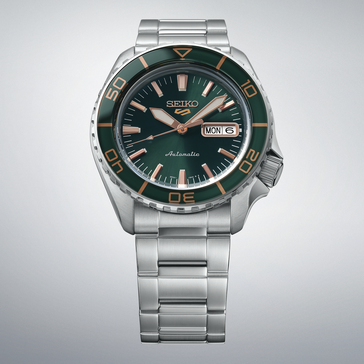 Seiko 5 Sports SKX HDB005 med en mörkgrön urtavla, matchande grön vridring, roséguldfärgade visare och index samt en länk i rostfritt stål, visad mot en ljusgrå bakgrund.