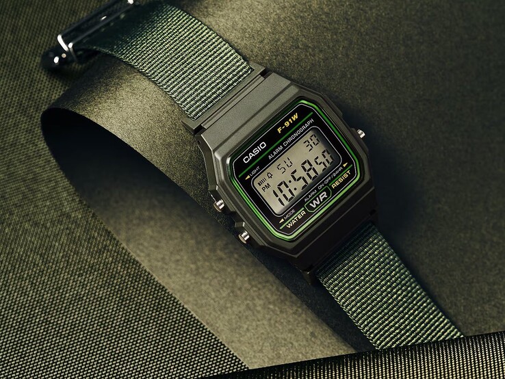 Casio F-91WF-3A digitalklocka med svart boett med gröna detaljer och vävd grön tygrem, fotograferad mot en mörkgrön strukturerad bakgrund.