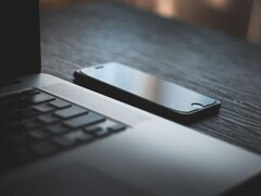 En smartphone som ligger bredvid en öppen bärbar dator på ett mörkt skrivbord