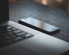 En smartphone som ligger bredvid en öppen bärbar dator på ett mörkt skrivbord