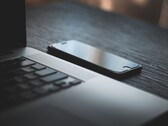 En smartphone som ligger bredvid en öppen bärbar dator på ett mörkt skrivbord