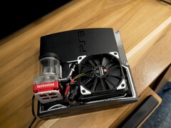 Anpassad vattenkyld PlayStation 3 med en röd SysCooling-pump och en stor svart fläkt monterad inuti höljet, placerad på ett träbord. (Bildkälla: Zac Builds via YouTube)
