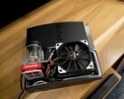 Anpassad vattenkyld PlayStation 3 med en röd SysCooling-pump och en stor svart fläkt monterad inuti höljet, placerad på ett träbord. (Bildkälla: Zac Builds via YouTube)