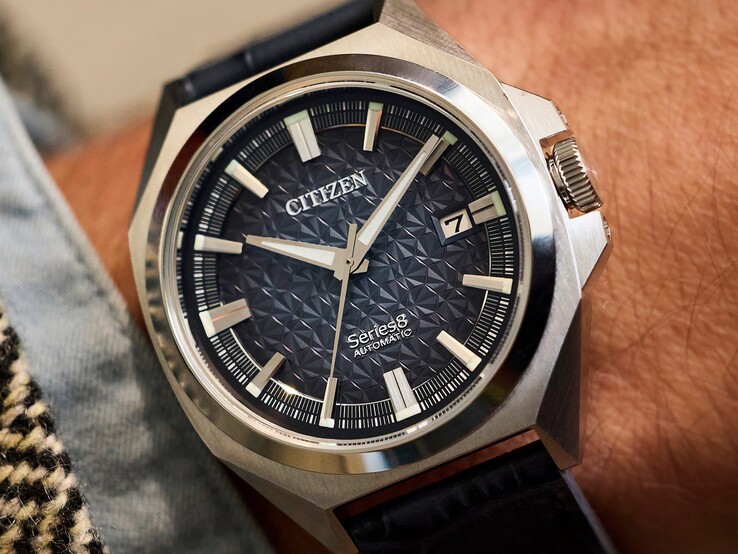 En automatisk klocka av modellen Citizen Series 8 831 med en geometrisk urtavla i bränd orange och brunt, guldfärgat boett och bezel samt ett integrerat guldfärgat H-länksarmband, bärd på en handled.