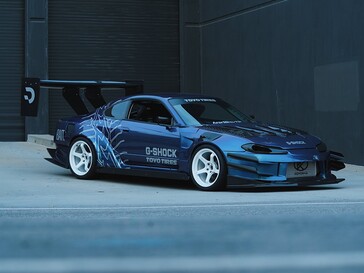 En blå driftbil med G-Shock- och Toyo Tires-motiv, parkerad utanför en industribyggnad.