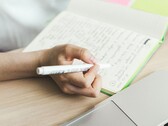 En person skriver anteckningar i en anteckningsbok bredvid en öppen bärbar dator