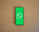 En smartphone på ett träbord som visar WhatsApps gröna startskärm med dess logotyp.