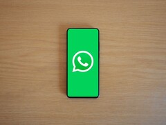 En smartphone på ett träbord som visar WhatsApps gröna startskärm med dess logotyp.