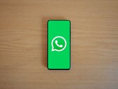 En smartphone på ett träbord som visar WhatsApps gröna startskärm med dess logotyp.